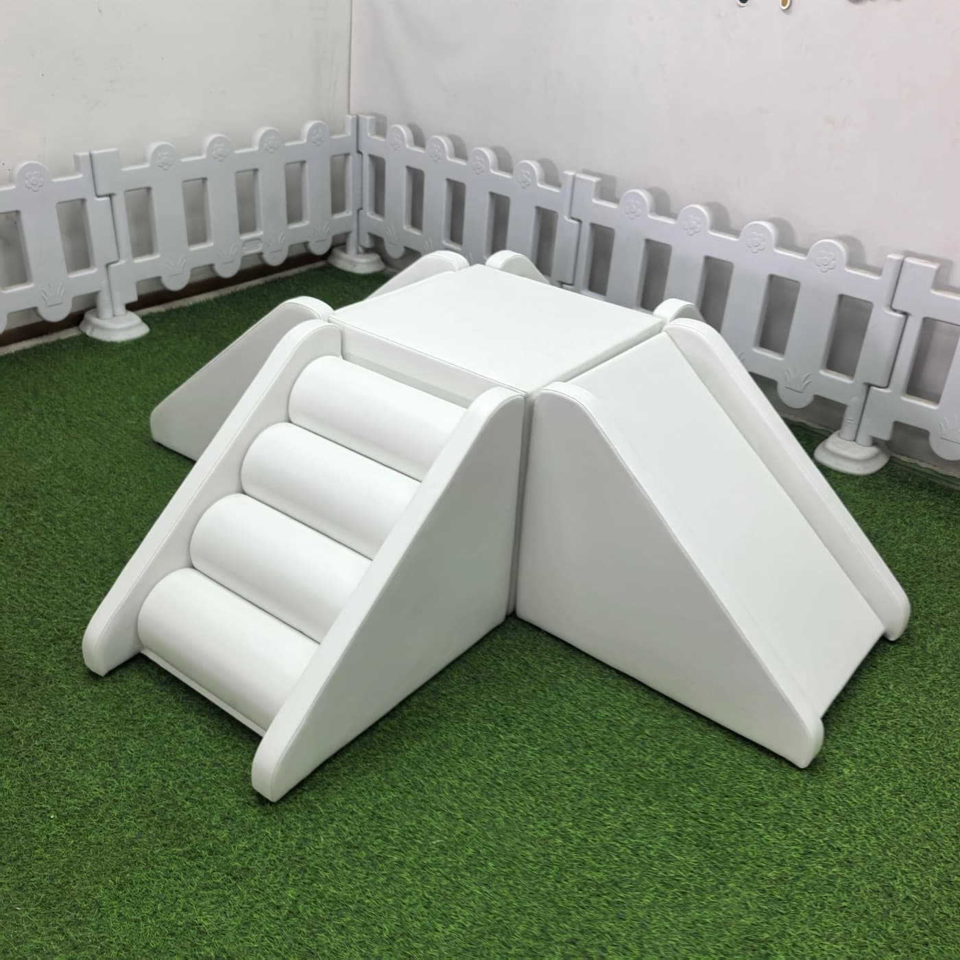 White soft-play set with a roller-step climber and a slide joined by a center platform